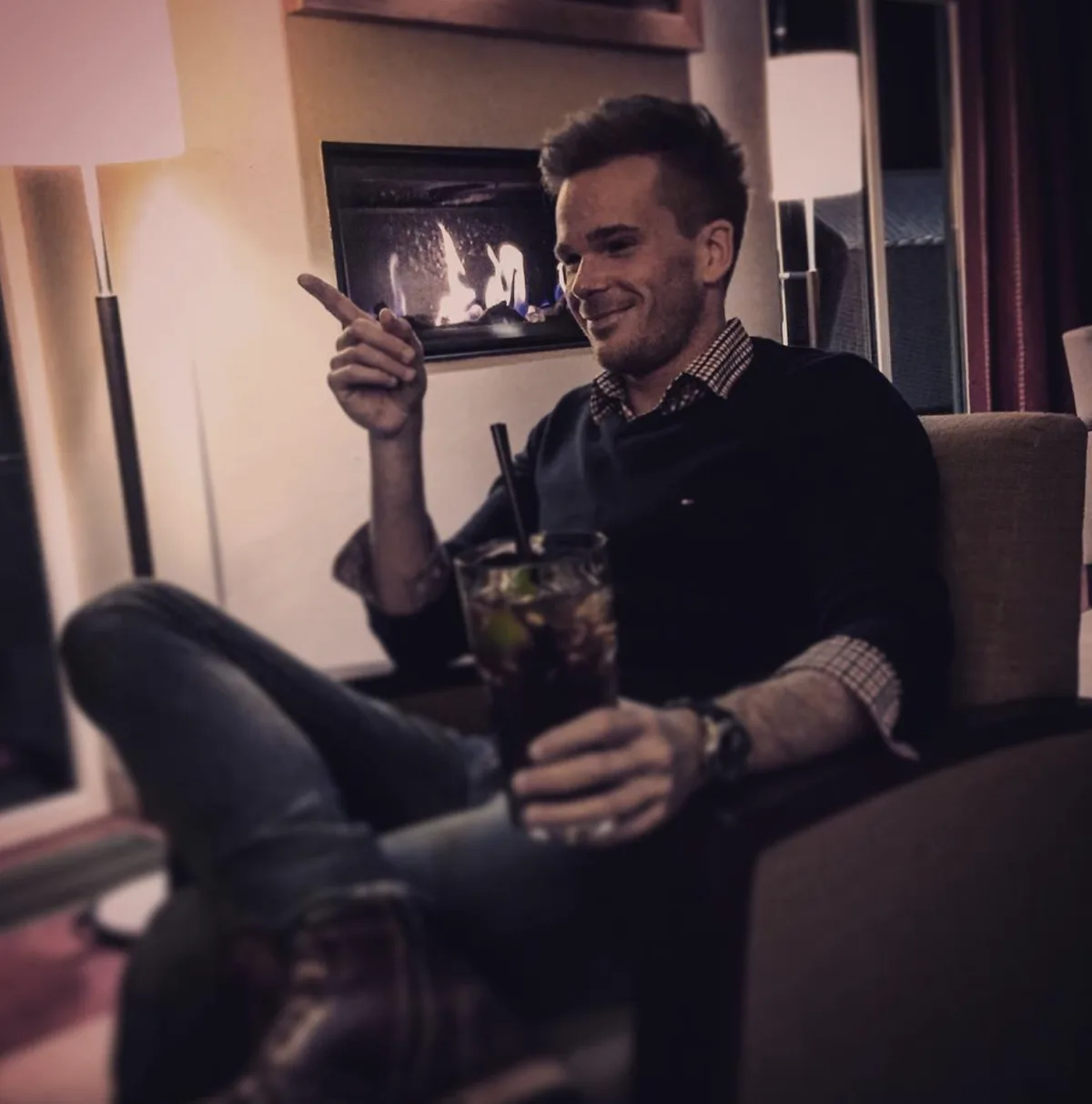 Marcel sitzt mit einem Getränk am Kamin