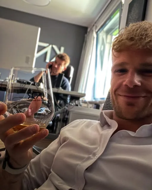 Marcel stößt im Büro mit einem Glas an